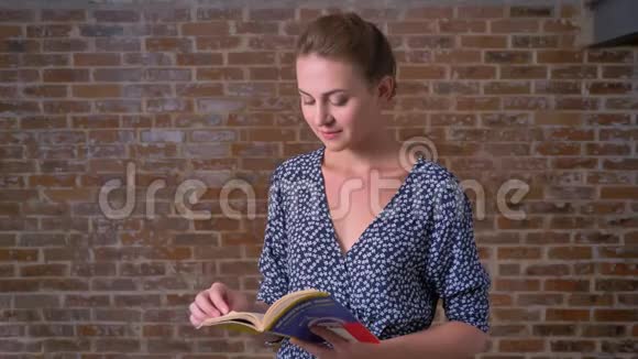 快乐平静的白种人黑发女人站直了看书看着砖墙上轻松的镜头视频的预览图