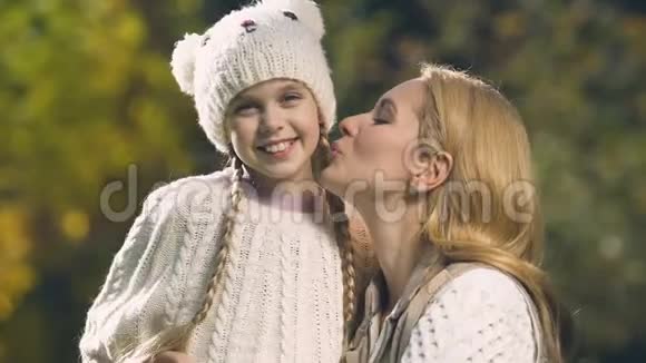 妈妈亲女儿的脸颊非常高兴的女孩在公园的镜头前微笑视频的预览图
