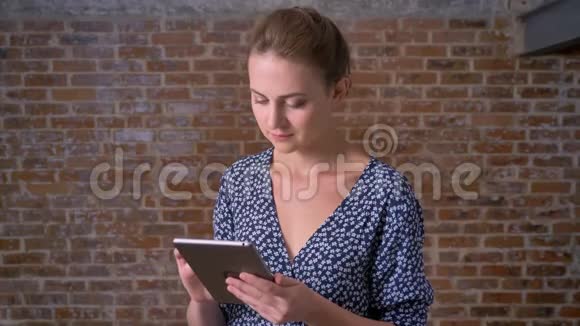 穿着蓝色连衣裙的可爱的深黑色白种人正在擦拭平板电脑看着镜头她很放松对砖头充满信心视频的预览图