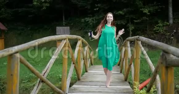 穿绿色衣服的女孩在木桥上用耳机跳舞4K视频的预览图