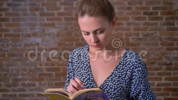 浓黑的白种人女性拿着书在砖背景上微笑着看着摄像机视频的预览图