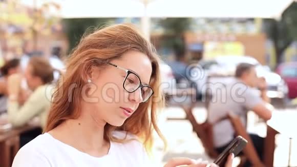 戴眼镜的漂亮女孩在户外咖啡馆上网视频的预览图