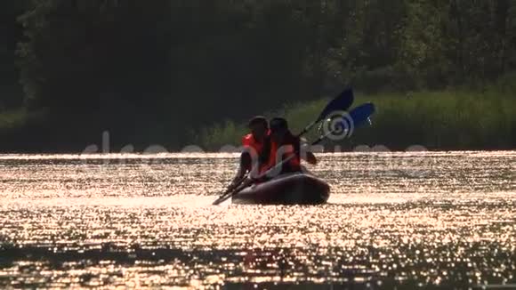 坐在皮划艇上划桨的男人和女孩被送往日落慢动作视频的预览图