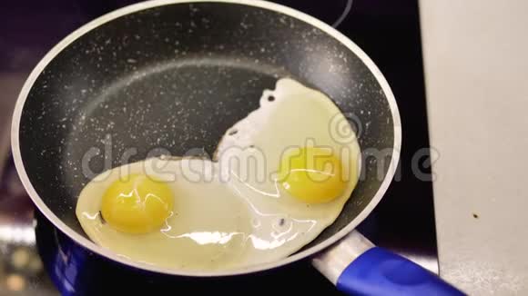两个鸡蛋在平底锅中用蓝色手柄煎俯视视频的预览图