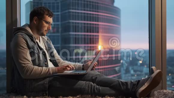 一个手提电脑的人正坐在摩天大楼的一层高楼的窗户旁视频的预览图