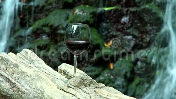一杯红酒矗立在背景的木制表面一块有瀑布的岩石上视频的预览图
