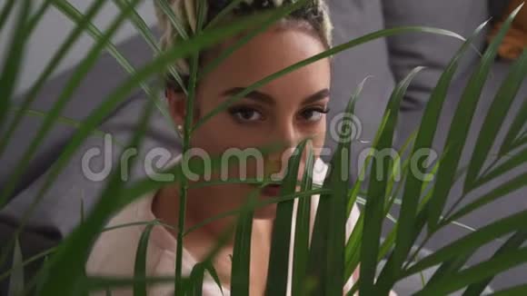 美丽性感的年轻女人大眼睛透过植物的叶子看视频的预览图
