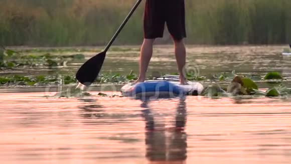 日落时人们站在充气筏上划桨板沿着河边划桨慢动作视频的预览图