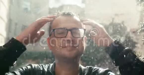 这位戴眼镜的英俊男子的特写肖像在雨中抬头摸着他的头发晴天4K录像视频的预览图