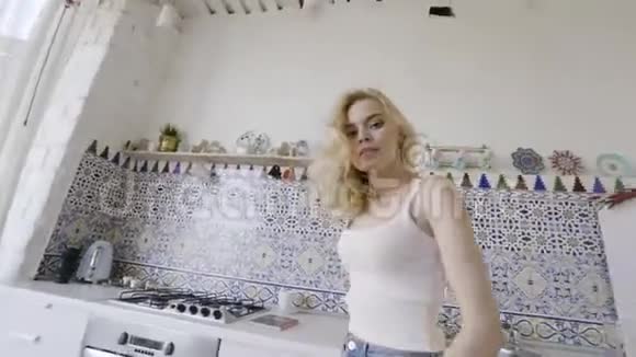 现代厨房里年轻金发女人的性感肖像行动厨房里性感的金发女郎看着站着的摄像机视频的预览图