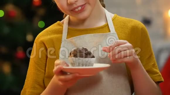 穿着围裙的女孩拿着纸杯蛋糕对着镜头微笑圣诞快乐的童年视频的预览图