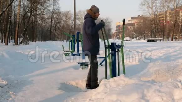 穿着带罩的蓝羽绒服的人在一个冬季城市公园里从事滑雪模拟器后景视频的预览图