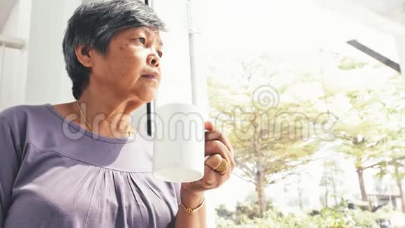 不高兴的孤独的亚洲老年妇女独自在家喝咖啡慢动作视频的预览图
