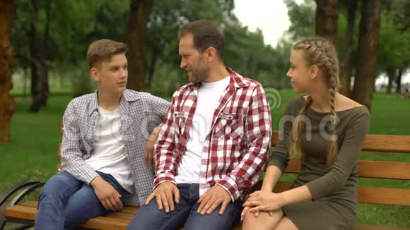 爸爸和他的男女青少年在公园的长椅上聊天放松视频的预览图