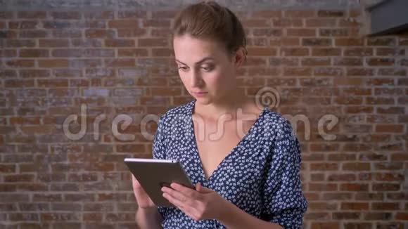 红黑肤色的白种人黑黑肤色的女孩正在擦着她的平板电脑开心地在红砖背景上微笑视频的预览图