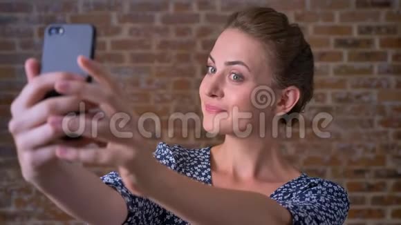 美丽的白种人深色的女性在砖房里站着一边自拍一边微笑视频的预览图