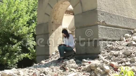 美丽的黑发正在阅读一本书坐在一座建筑的废墟上视频的预览图