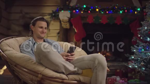 圣诞夜年轻人在智能手机上发短信用装饰好的树笑视频的预览图