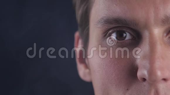 集中精力的年轻人半张脸的肖像睁开眼睛看着黑色背景的镜头视频的预览图