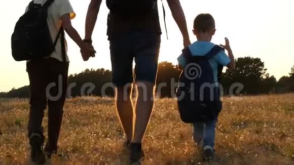 游客的幸福家庭爸爸和他的两个儿子在日落时背着背包在大自然中行走的概念视频的预览图
