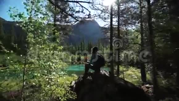 一位年轻的女游客坐在一块大石头上坐在风景如画的蓝色湖泊上在山上滑了50英尺视频的预览图