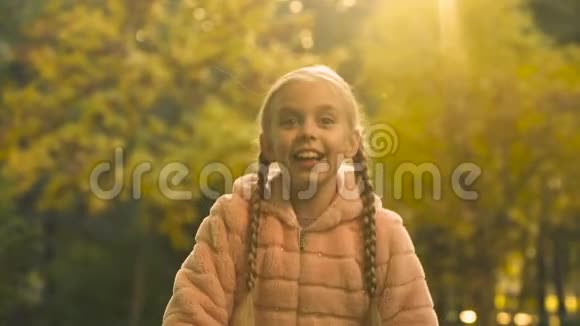 可爱的女孩穿着毛皮大衣扔掉秋叶无忧无虑快乐的童年视频的预览图