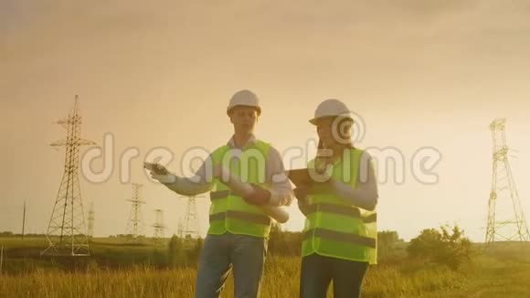 两名电工一起工作戴着头盔站在输电线路附近的田野里站在视频的预览图