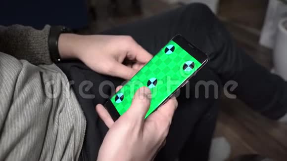 在家用智能手机帅特写一个男人手拿着一部带有垂直绿色屏幕的移动电话视频的预览图