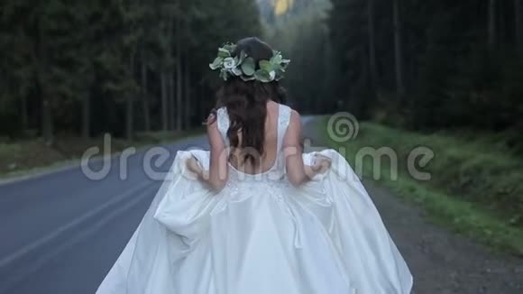 新娘头上戴着绿冠在靠近森林的道路上奔跑慢动作视频的预览图