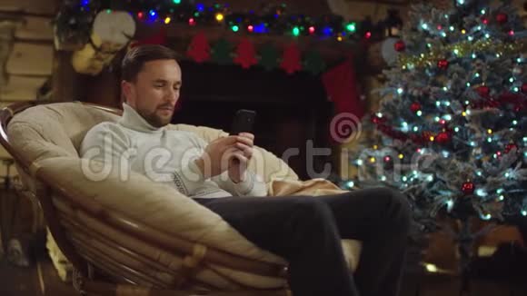 圣诞夜成年男子在智能手机上发短信用装饰好的树笑视频的预览图