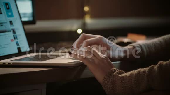 女孩的手放在笔记本电脑上特写镜头穿毛衣的女人在家里黑暗中上网娱乐4K视频的预览图