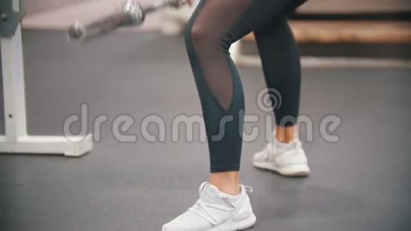 一个正在健身房训练腿脚的女人手里拿着一个铁哑铃身体向下倾视频的预览图