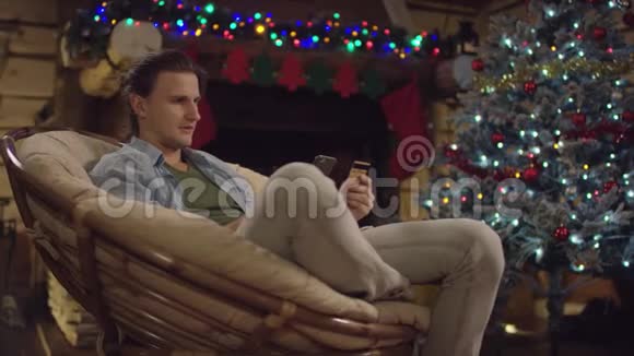 年轻的长发男子在圣诞夜用智能手机和信用卡在网上商店买了一个礼物视频的预览图