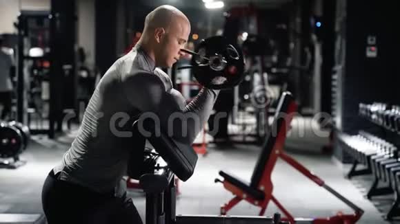 运动服训练的肌肉男在健身房用杠铃做二头肌运动视频的预览图