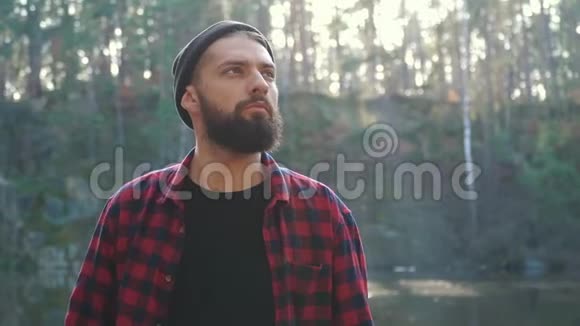 一个带着斧头在森林里散步的留胡子的年轻人在户外用斧子清除森林视频的预览图
