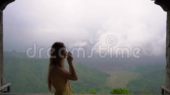 一名年轻女子在山上的一家咖啡馆喝茶或咖啡观看巴图山和视频的预览图