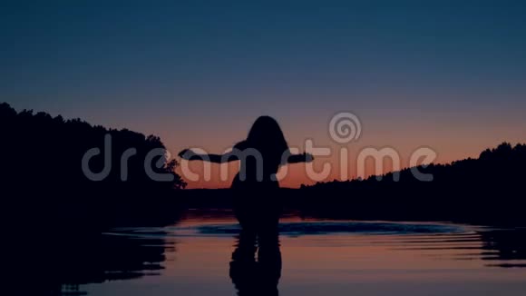 夕阳西下的湖中女人的剪影深深地站着膝盖溅起水花视频的预览图