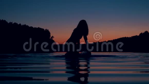 夕阳西下的湖中女人的剪影深深地站着膝盖溅起水花视频的预览图