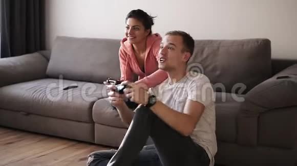年轻夫妇在家玩电子游戏坐在沙发上男人在地板上享受在一起玩游戏的时光视频的预览图