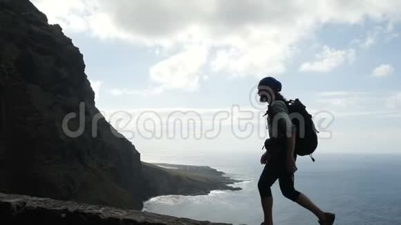 带背包的男性徒步旅行者正走在位于大洋上方的金丝雀岛上的一条道路边缘视频的预览图