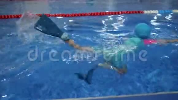 戴着护目镜泳衣帽和脚蹼的小女孩正在游泳池里训练游泳视频的预览图