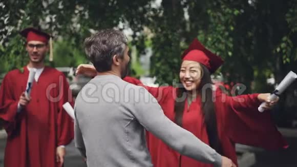快乐的女儿即将毕业的学生正在拥抱她慈爱的父亲胡须男笑着女孩拿着文凭拿着文凭视频的预览图