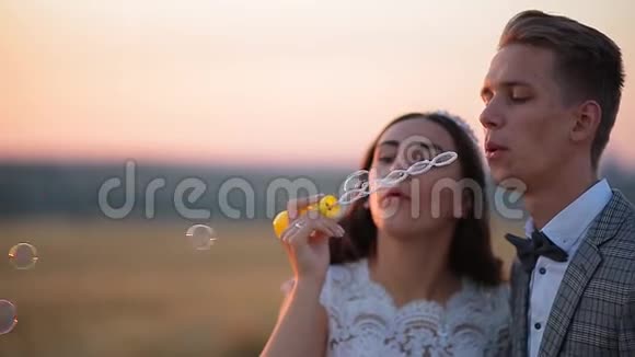 美丽的新娘和新郎在日落时分在公园里笑着吹肥皂泡视频的预览图