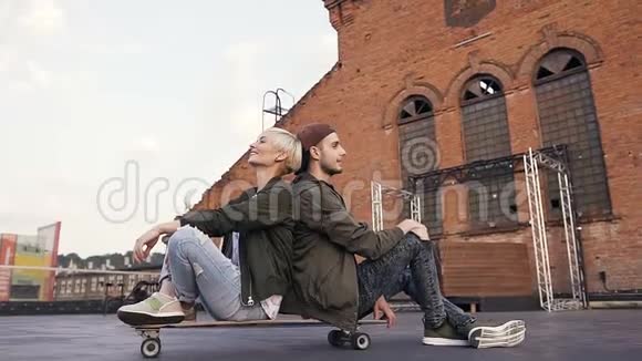 年轻漂亮的夫妇正在大街上的长板上互相坐在一起玩年轻的白种人视频的预览图