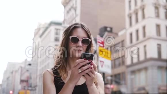 快乐体贴的欧洲女性美容博主戴着太阳镜使用智能手机购物应用程序在纽约慢动作视频的预览图