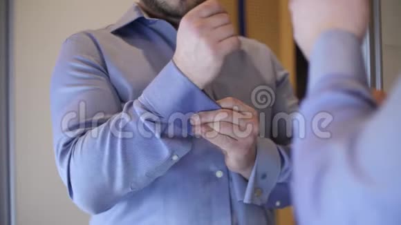 一个穿蓝色衬衫的人把袖扣系在衬衫上视频的预览图