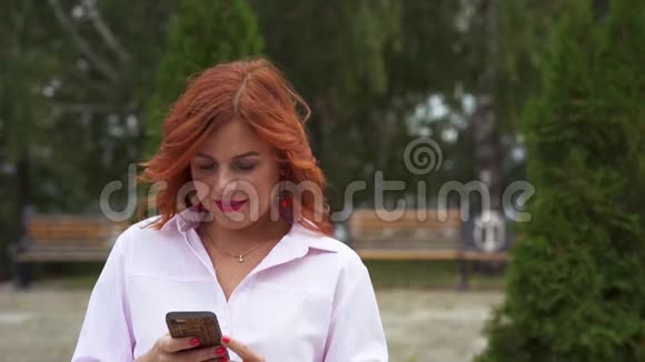 一位红头发的中年妇女正在看她的智能手机上的留言视频的预览图