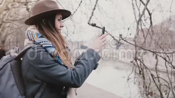 年轻快乐的旅行者女孩带着背包拍着智能手机照片在罗马的飞机树下沿着河岸散步视频的预览图