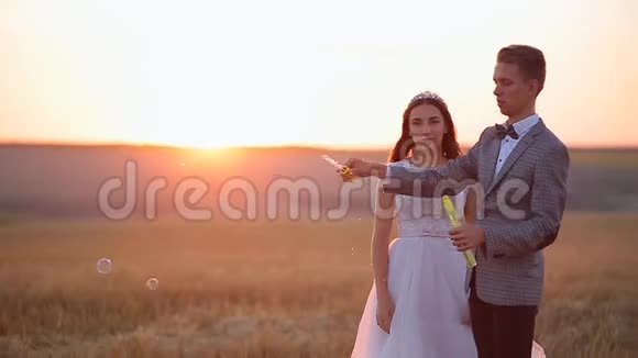 美丽的新娘和新郎在日落时分在公园里笑着吹肥皂泡视频的预览图