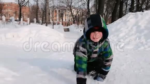男孩在雪地里玩耍在冬季城市公园的雪堆中沿着雪道爬行视频的预览图